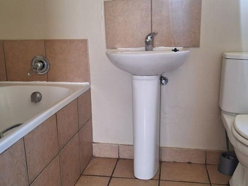 A functional bathroom featuring a pedestal basin, built-in bathtub, and close-coupled toilet with neutral ceramic tiling.