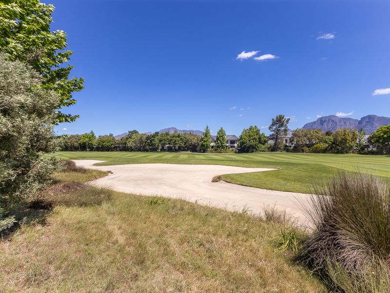 A scenic view overlooking a well-maintained golf course with a sand bunker, lush green fairways, and mountain vistas in the background.
