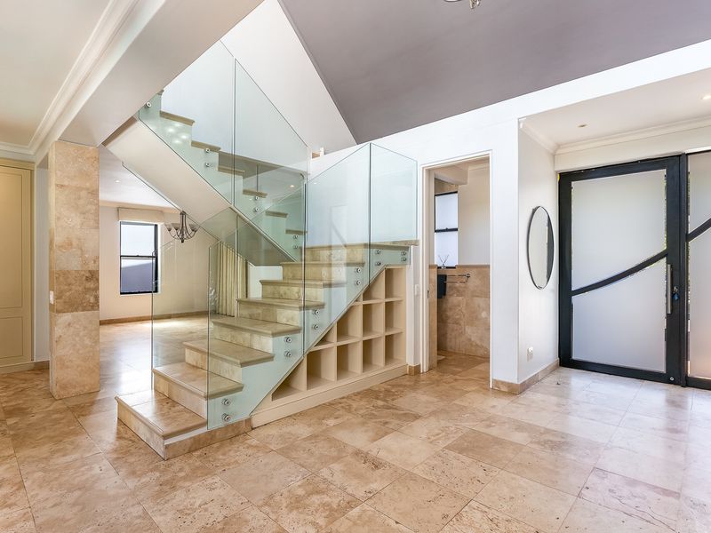 Spacious entrance hall featuring elegant travertine flooring, a modern staircase with glass balustrades, and integrated under-stair storage.