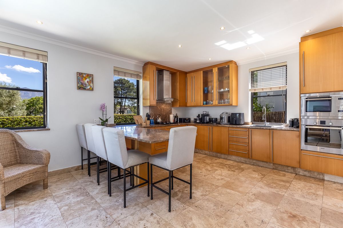 A well-lit kitchen featuring wooden cabinetry, granite countertops, integrated stainless steel appliances, and natural stone flooring with a breakfast bar area.