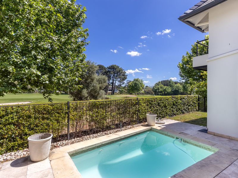 A private plunge pool set within a stone-paved patio area, featuring a metal fence and views overlooking the adjacent golf course.