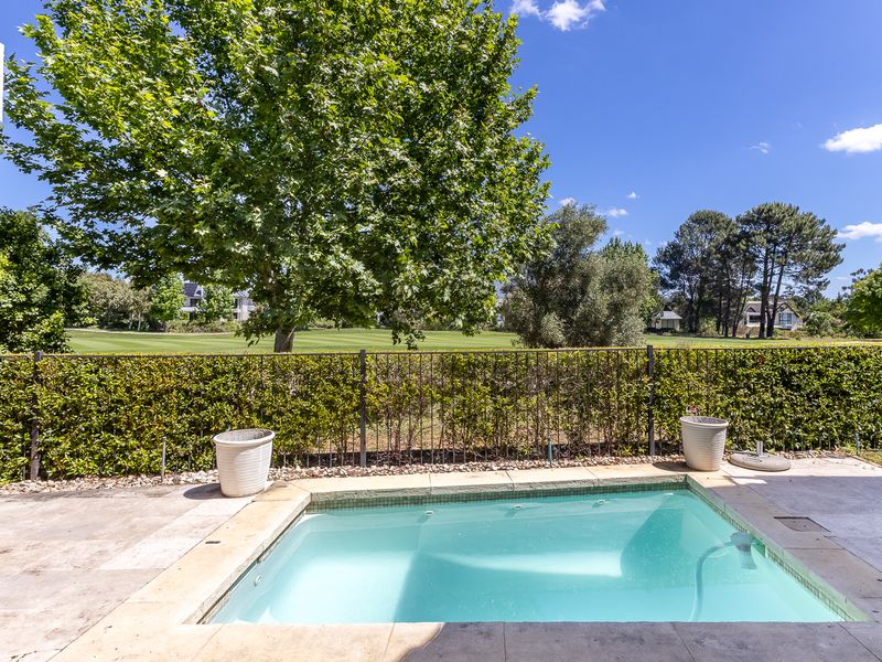 A well-maintained swimming pool area featuring stone paving and a metal fence, overlooking a lush green golf course landscape.