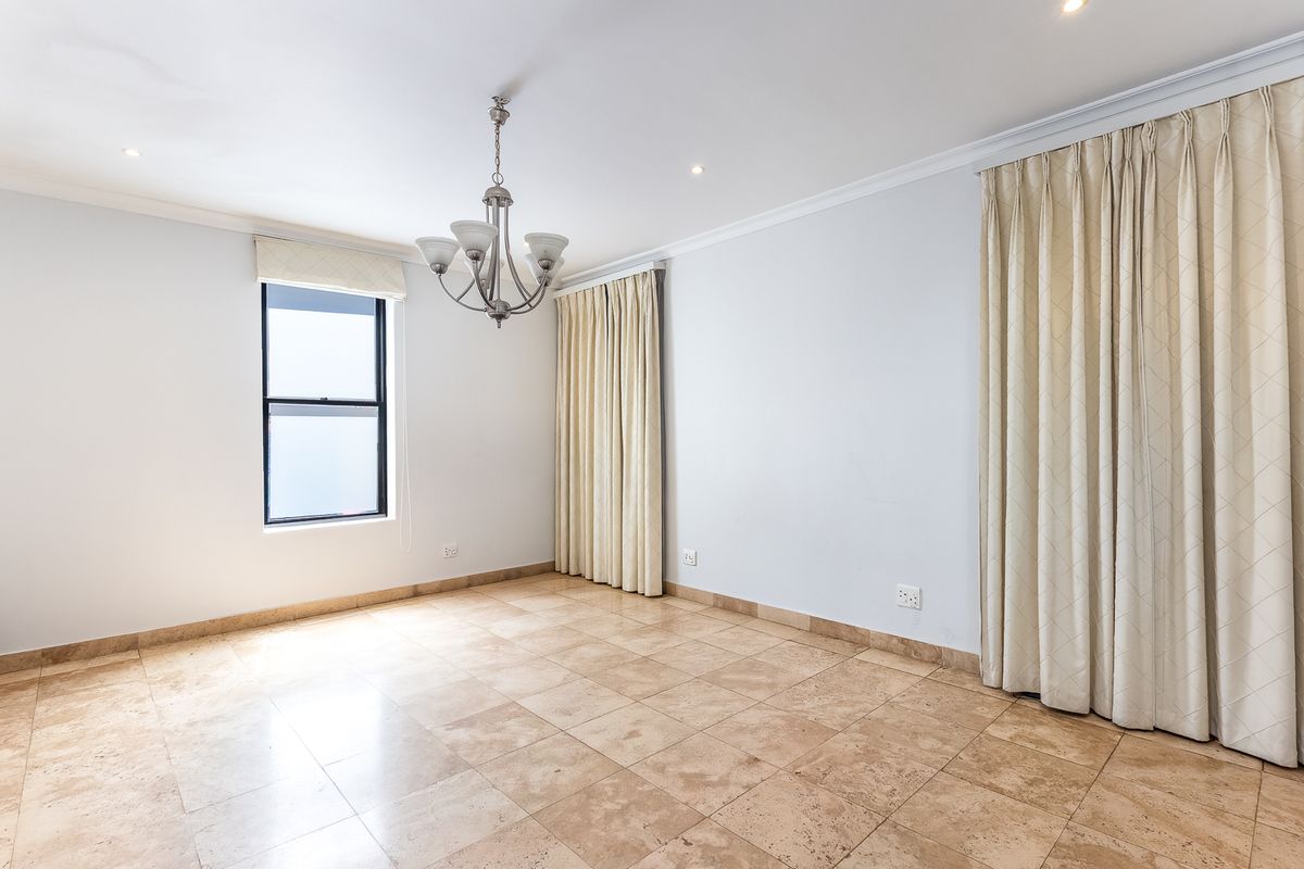 A bright and spacious bedroom featuring neutral travertine tile flooring, elegant cornicing, and a central chandelier, offering a clean canvas for personalization.