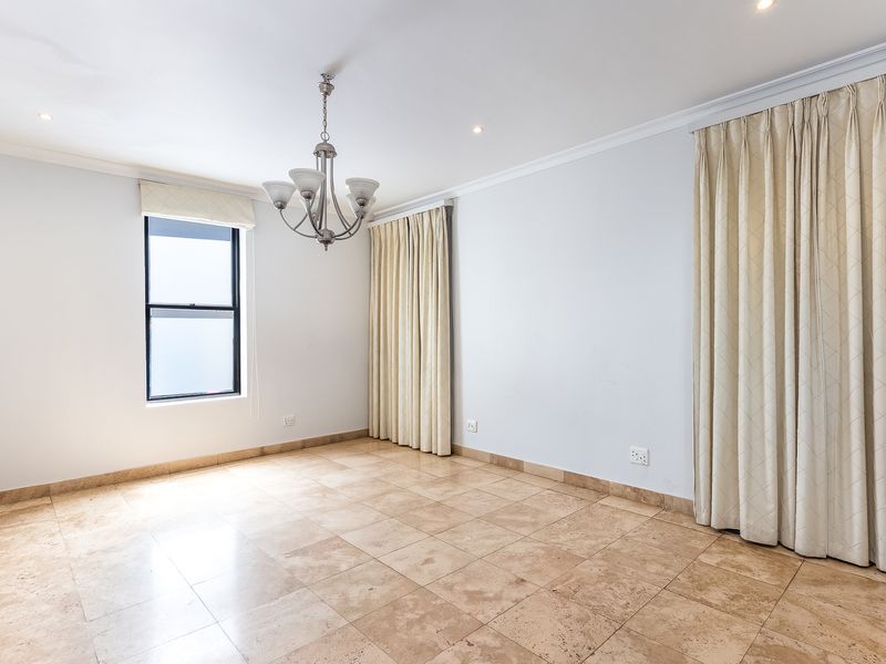 A bright and spacious bedroom featuring neutral travertine tile flooring, elegant cornicing, and a central chandelier, offering a clean canvas for personalization.