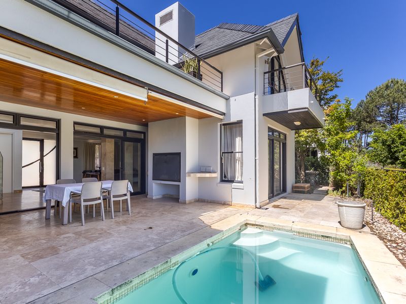 A well-maintained outdoor entertainment area featuring a swimming pool, covered patio with timber ceiling, and a built-in braai, perfect for alfresco dining.