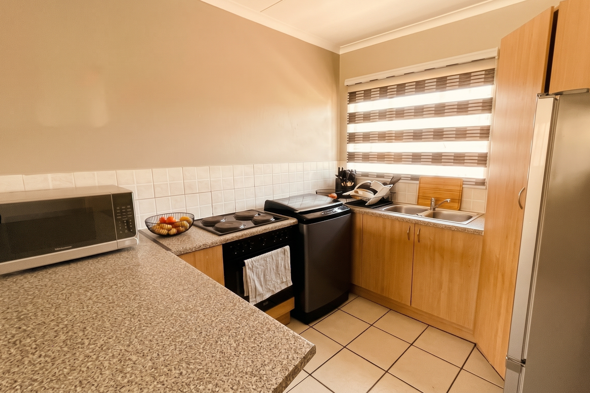 A functional kitchen featuring laminate countertops, tiled backsplash, built-in oven, electric hob, and double sink with ample cabinetry and tiled flooring.
