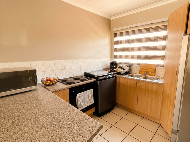A functional kitchen featuring laminate countertops, tiled backsplash, built-in oven, electric hob, and double sink with ample cabinetry and tiled flooring.