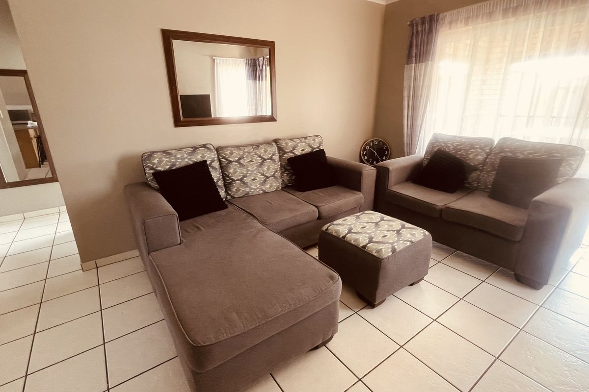 A living room featuring neutral wall tones, tiled flooring, and a sliding glass door providing natural light.