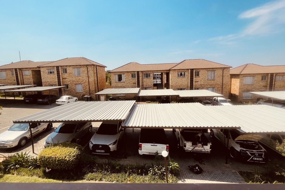 An elevated view of the apartment complex parking area featuring multiple carports and paved driveways between the brick residential buildings.