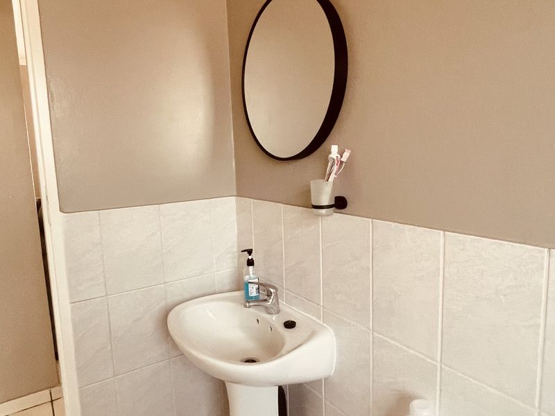 A functional bathroom featuring a pedestal basin, wall-mounted mirror, and tiled finishes, providing a clean and practical space.