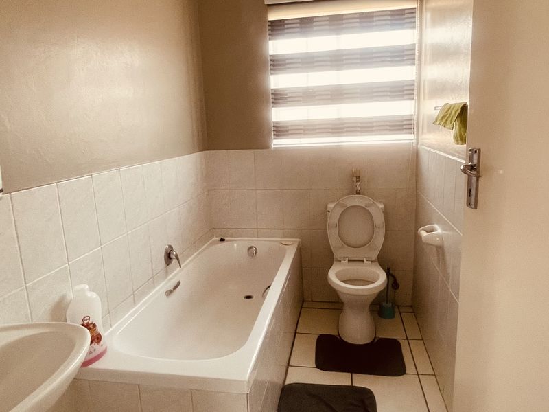 A functional bathroom featuring a built-in bathtub, pedestal basin, and toilet with neutral wall finishes and tiled flooring.