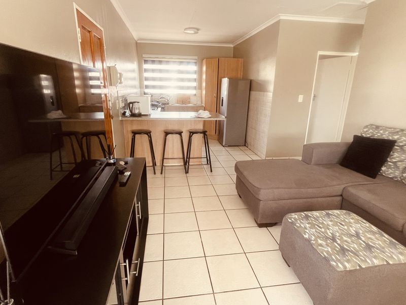 An open-plan living and kitchen area featuring tiled flooring, a breakfast bar, and functional kitchen cabinetry.