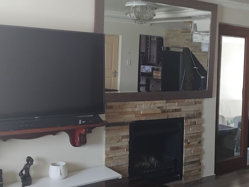 Living room featuring a stone-clad fireplace, built-in mirror, and staircase access, providing a functional and cozy focal point for the home.
