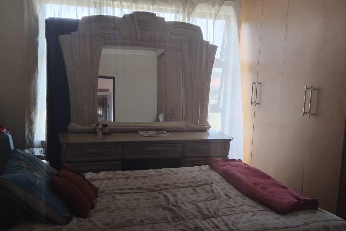 A bedroom featuring built-in cupboards and a large window, providing natural light. The space is functional with standard finishes.