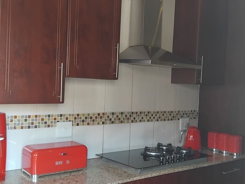 A functional kitchen featuring dark wood cabinetry, granite countertops, a built-in gas hob, and a stainless steel extractor fan with a decorative tiled backsplash.