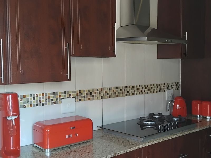 A functional kitchen featuring dark wood cabinetry, granite countertops, a gas hob with a stainless steel extractor fan, and a decorative mosaic tile backsplash.