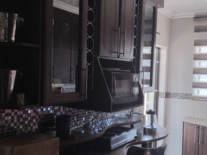 A functional kitchen featuring dark wood cabinetry, granite countertops, a mosaic tile backsplash, and a built-in microwave with modern roller blinds.