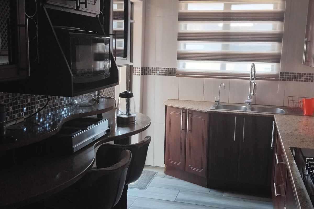 A functional kitchen featuring dark wood cabinetry, granite countertops, a mosaic tile backsplash, and integrated appliances including a cooktop and microwave.