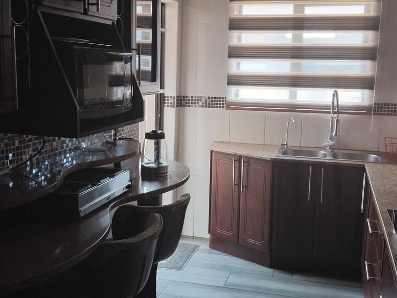 A functional kitchen featuring dark wood cabinetry, granite countertops, a mosaic tile backsplash, and integrated appliances including a cooktop and microwave.