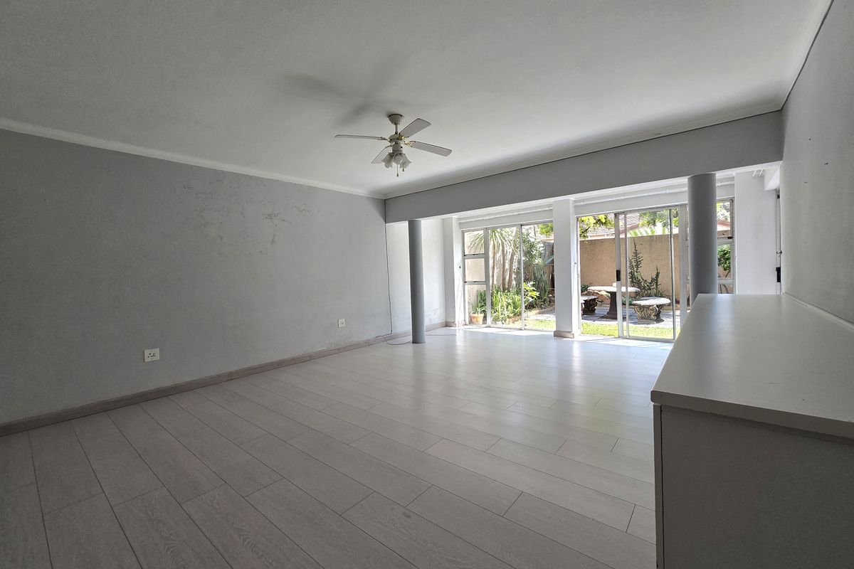 Spacious, light-filled living area featuring modern laminate flooring, a ceiling fan, and large sliding glass doors providing direct access to the rear garden.