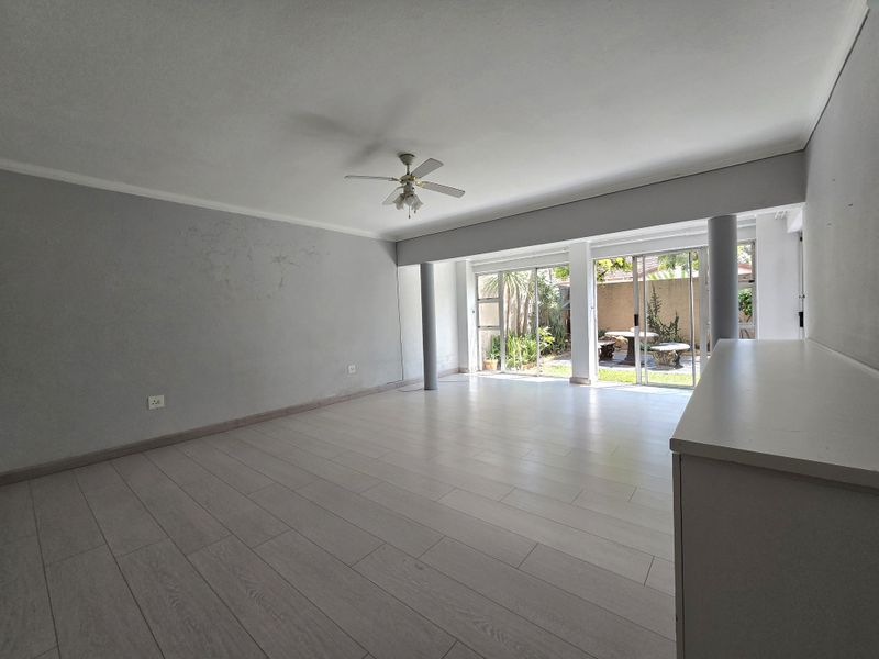 Spacious, light-filled living area featuring modern laminate flooring, a ceiling fan, and large sliding glass doors providing direct access to the rear garden.