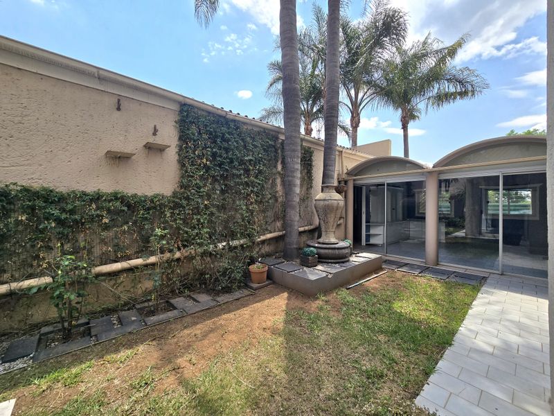 A private rear garden area featuring a stone fountain, tiled pathway, and large sliding glass doors providing access to the interior living space.