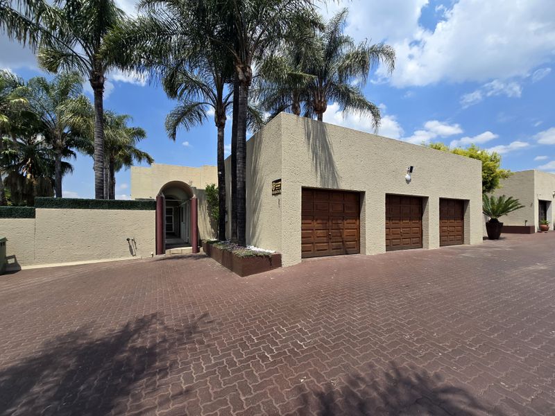 Front exterior view of the property featuring a triple garage, paved driveway, and a distinctive arched entrance with mature palm trees.