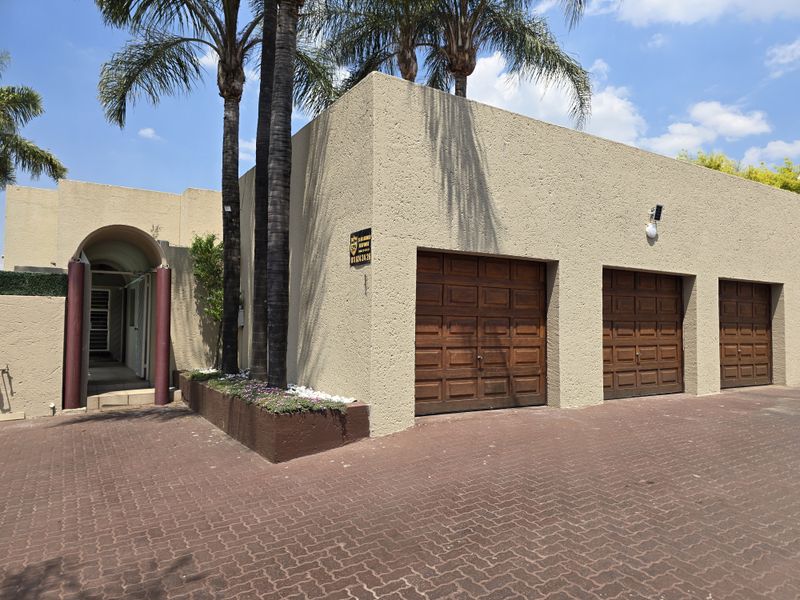 Front elevation of a house featuring a triple garage with wooden doors, a paved driveway, and an arched entrance with mature palm trees.