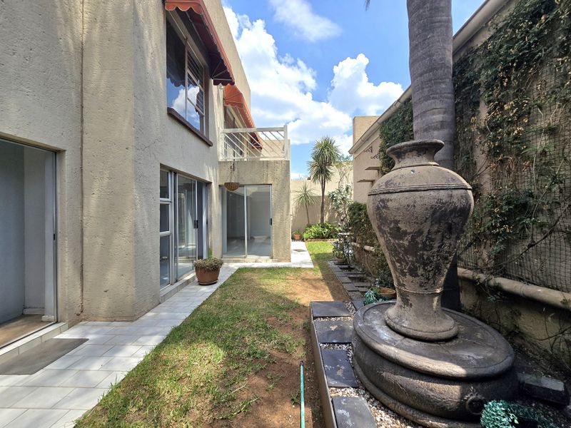 Rear exterior view of the property featuring a small garden, tiled patio area, sliding glass doors, and a stone fountain feature.