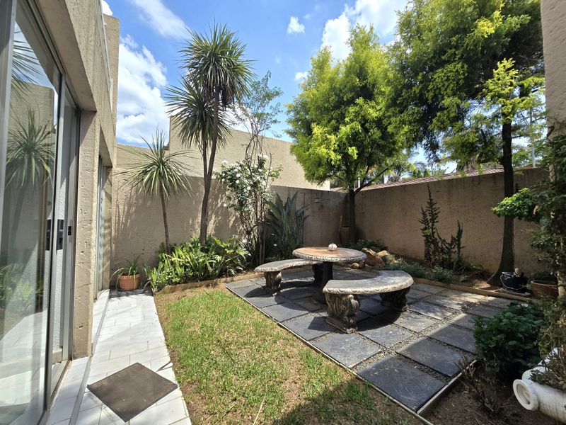A private rear courtyard featuring a paved patio area, established garden beds, and direct access to the home via sliding glass doors.