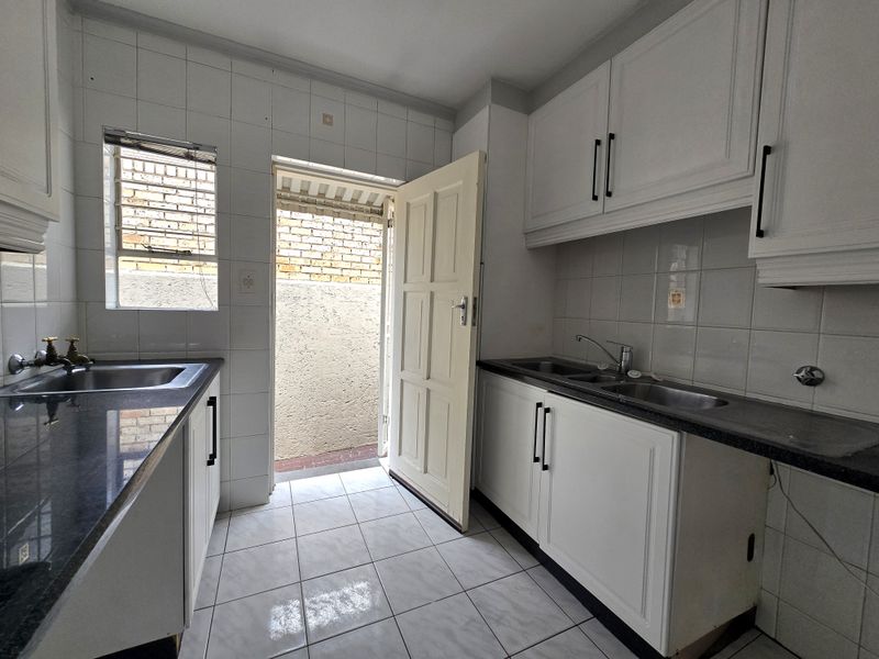 A functional kitchen featuring white cabinetry, granite countertops, double stainless steel sinks, and direct access to an exterior area.