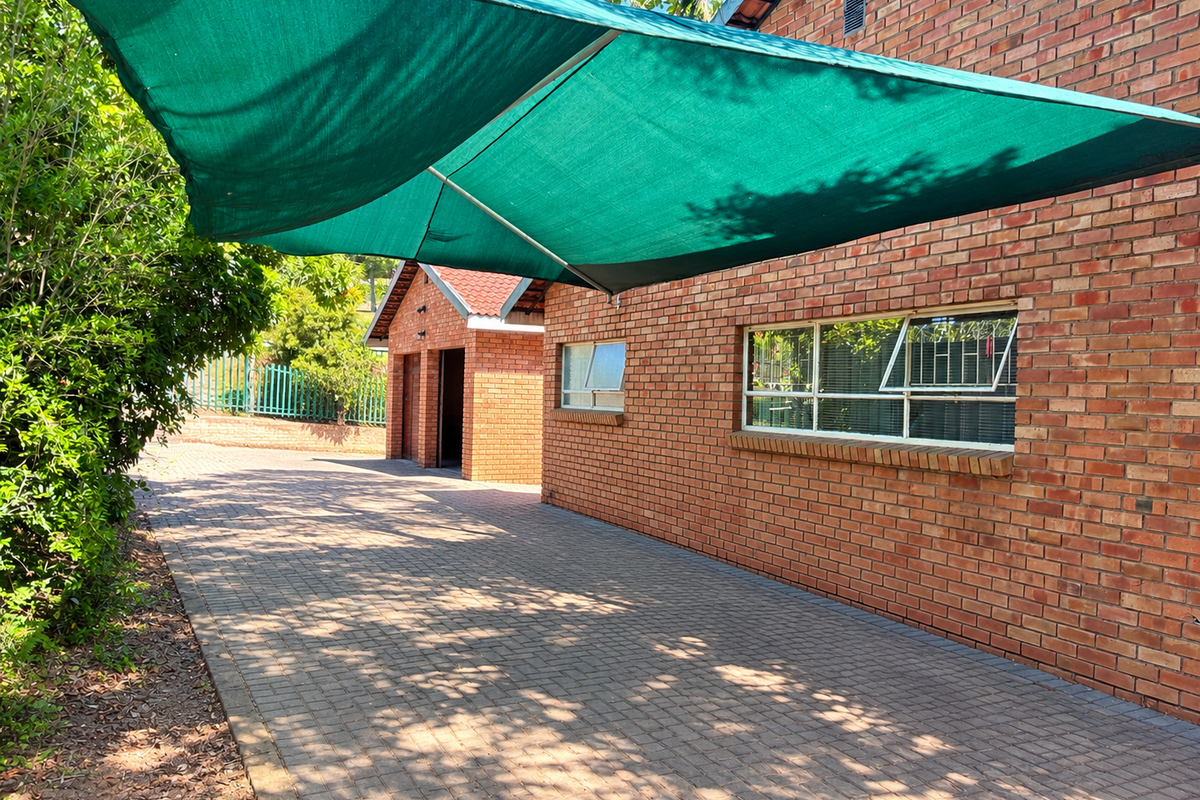 Rear exterior view featuring a brick facade, paved driveway, and a large green shade sail providing cover over the outdoor area.