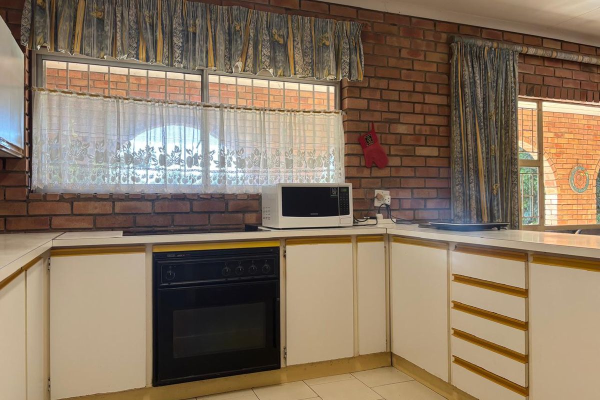 A dated kitchen featuring exposed brick walls, white cabinetry with yellow trim, built-in oven, and tiled flooring.