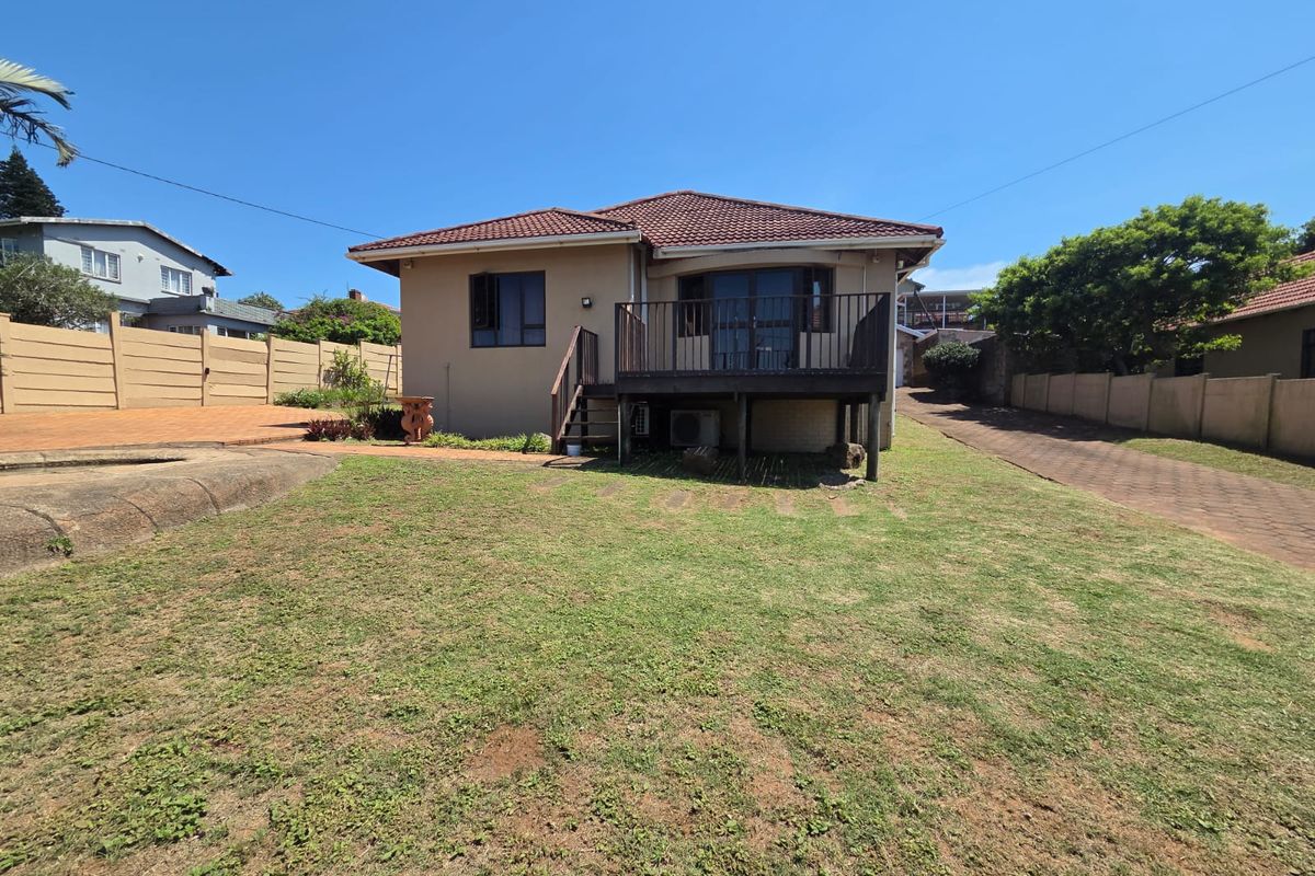 Rear view of the house featuring a raised timber deck with metal balustrades, a paved driveway, and a spacious garden area.