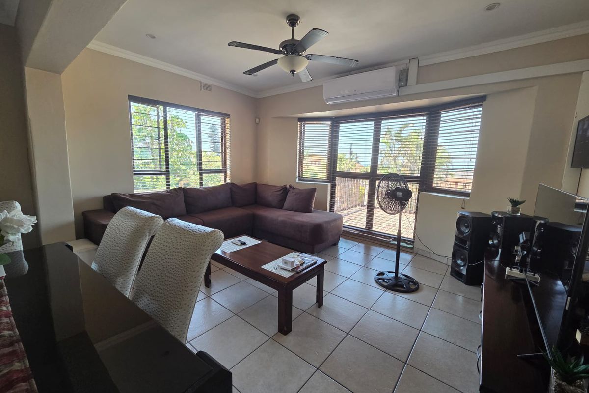 A spacious living room featuring tiled flooring, a ceiling fan, and a split-system air conditioner, with large windows and sliding doors providing natural light.