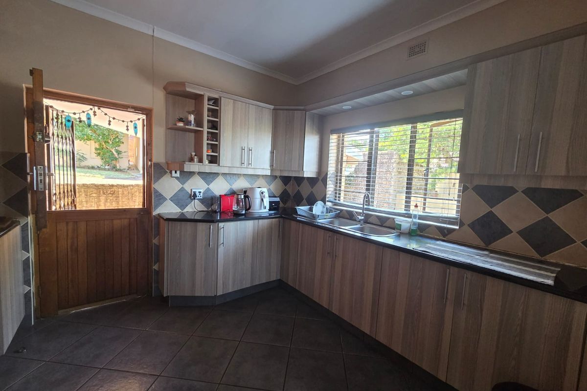 A functional kitchen featuring wood-look laminate cabinetry, granite countertops, tiled backsplash, and direct access to the exterior via a timber door.