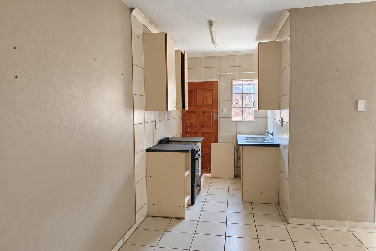 A compact, empty kitchen featuring tiled flooring, built-in cabinetry, a stainless steel sink, and a freestanding stove, requiring minor repairs and cosmetic updates.