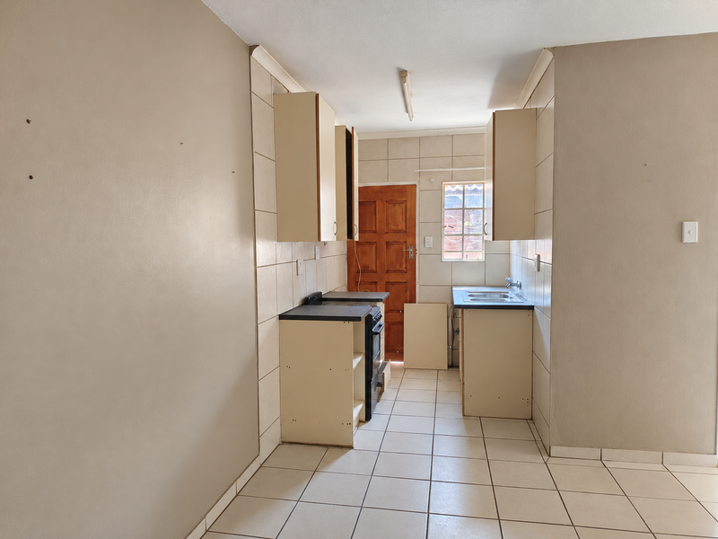 A compact, empty kitchen featuring tiled flooring, built-in cabinetry, a stainless steel sink, and a freestanding stove, requiring minor repairs and cosmetic updates.