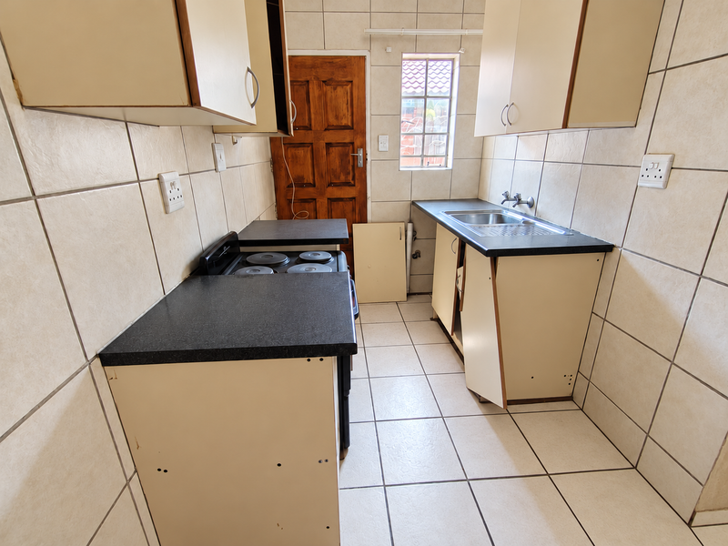 A compact kitchen featuring tiled walls and floors, built-in cabinetry, and a stainless steel sink, currently requiring maintenance and cosmetic repairs.