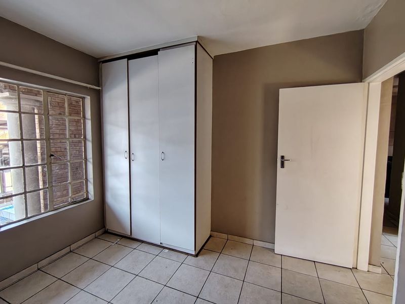 A functional bedroom featuring tiled flooring, a built-in wardrobe, and a window with security bars, offering a neutral canvas for personalization.