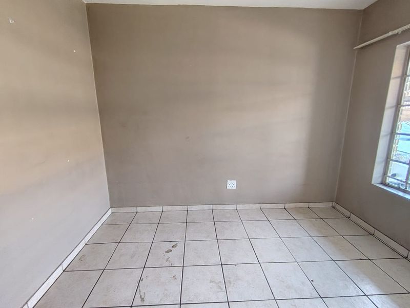 An empty bedroom featuring tiled flooring and a window with security bars, requiring minor cosmetic updates to improve its overall condition.