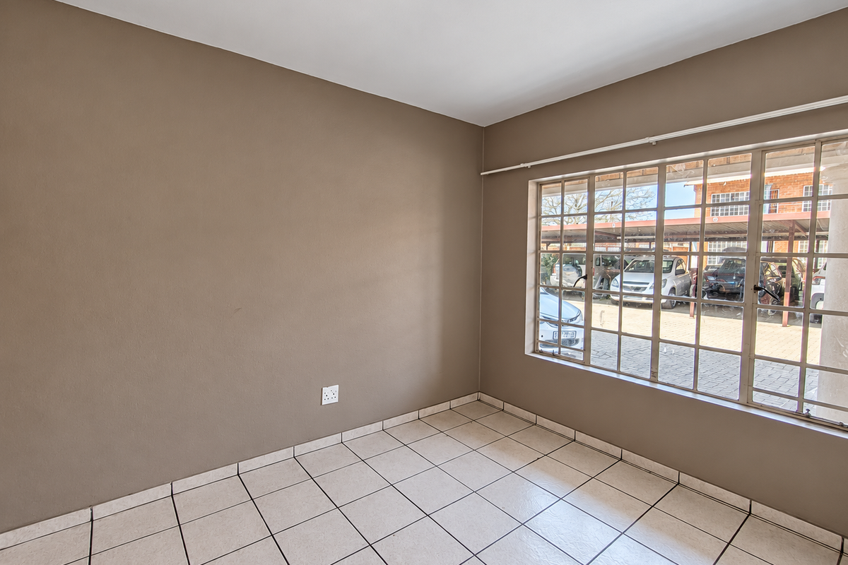 An empty bedroom featuring neutral wall paint, tiled flooring, and a large window with security bars, offering a blank canvas for personalization.