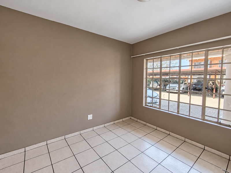 An empty bedroom featuring neutral wall paint, tiled flooring, and a large window with security bars, offering a blank canvas for personalization.