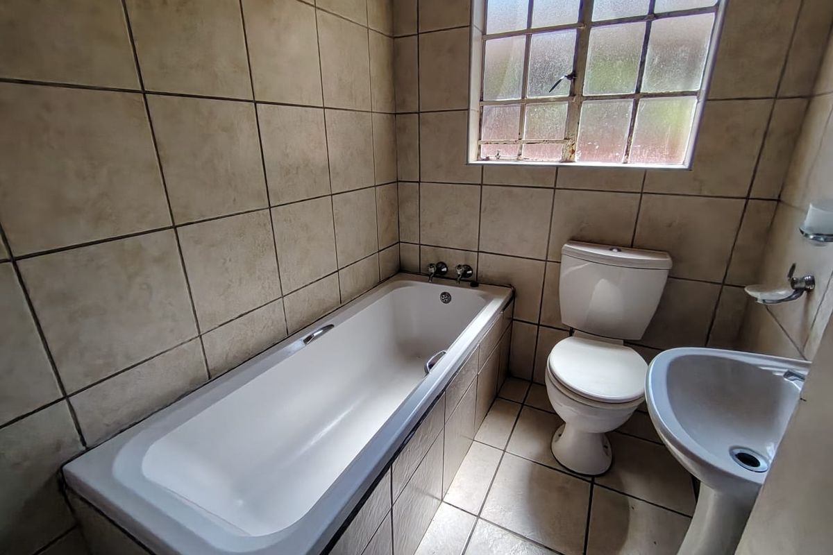 A compact bathroom featuring a bathtub, pedestal basin, and toilet with full-height wall tiling and a window for natural light.