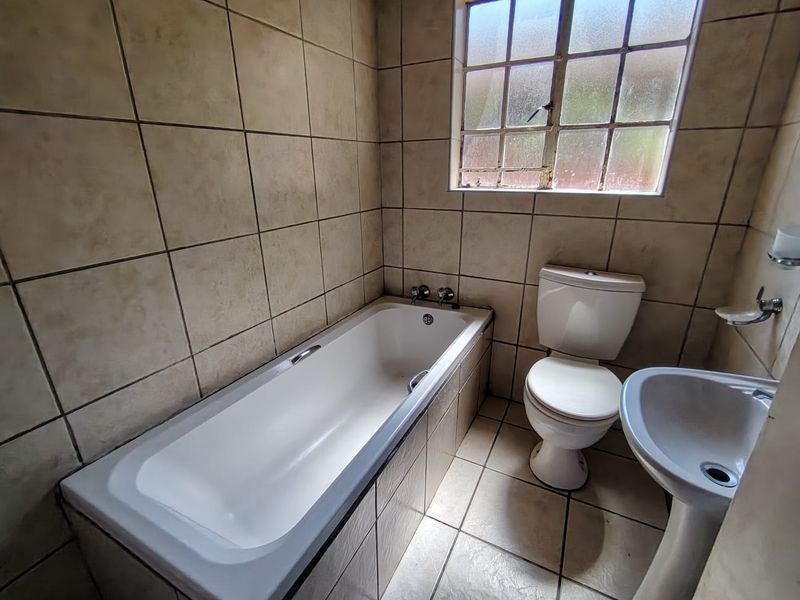 A compact bathroom featuring a bathtub, pedestal basin, and toilet with full-height wall tiling and a window for natural light.