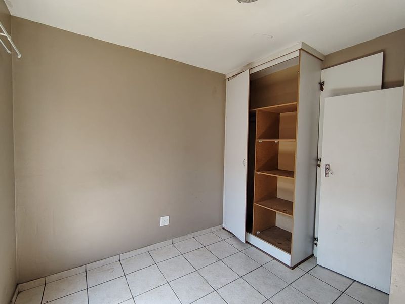 A vacant bedroom featuring tiled flooring and a built-in cupboard with visible wear to the cabinetry and wall finishes.