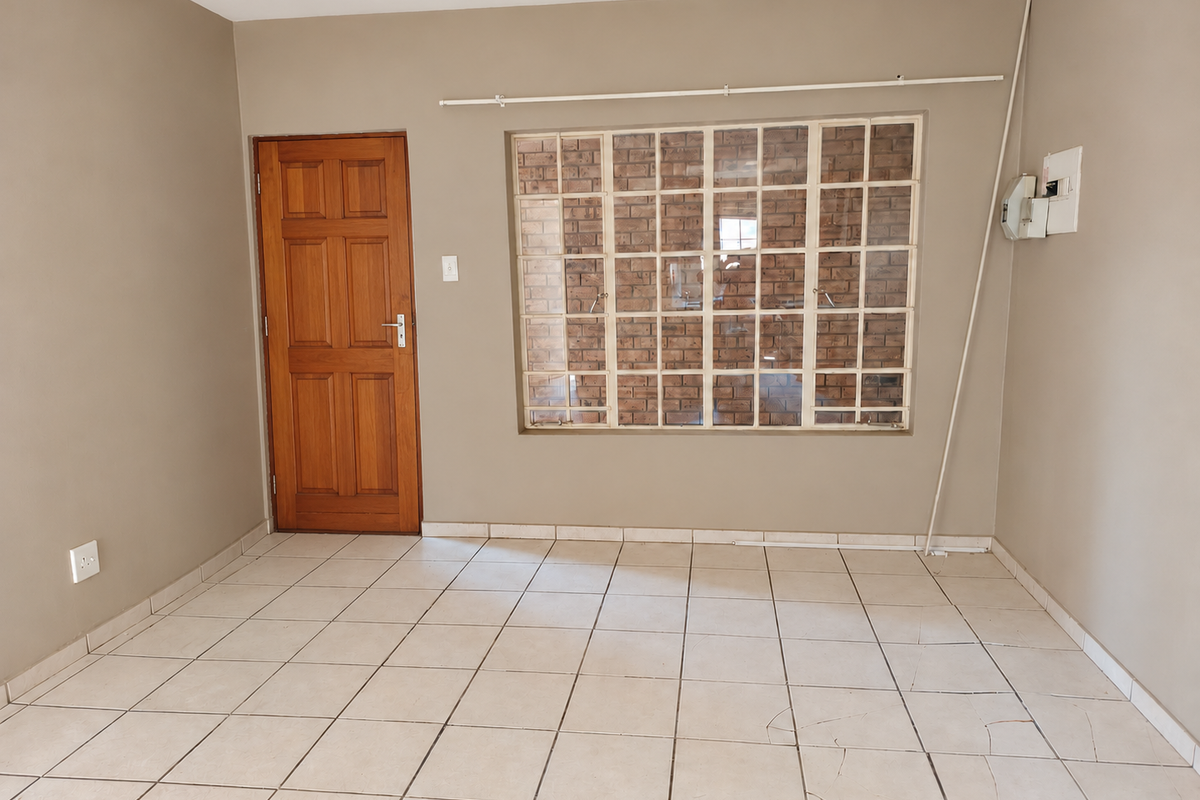 An empty living room featuring neutral wall paint, tiled flooring with visible cracks, a wooden door, and a large grid window.