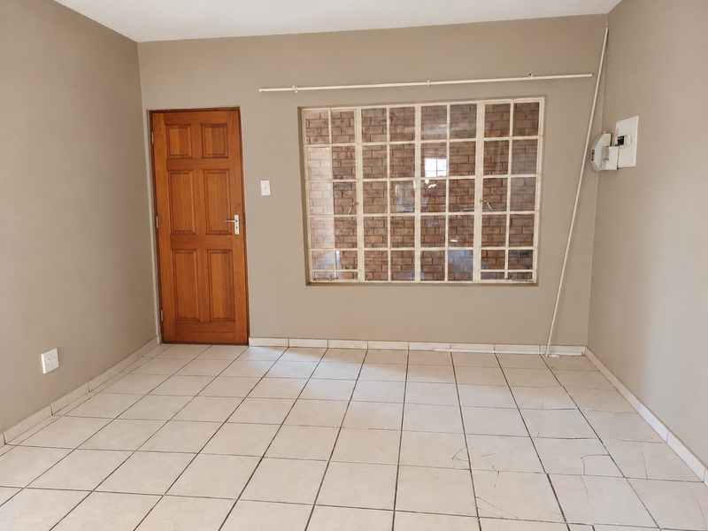 An empty living room featuring neutral wall paint, tiled flooring with visible cracks, a wooden door, and a large grid window.