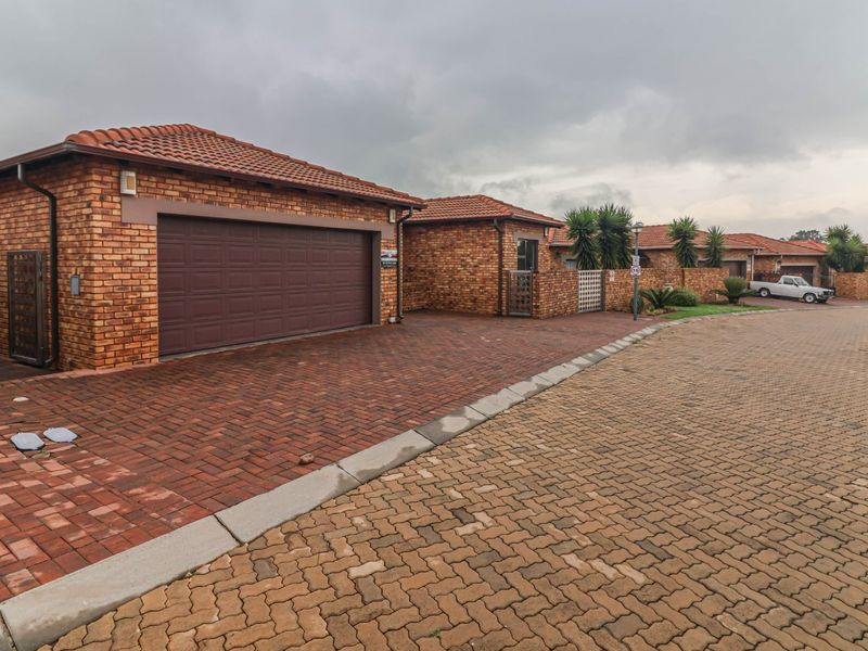 A street-level view of a cluster home featuring a face brick exterior, tiled roof, and a private paved driveway with an automated garage door.