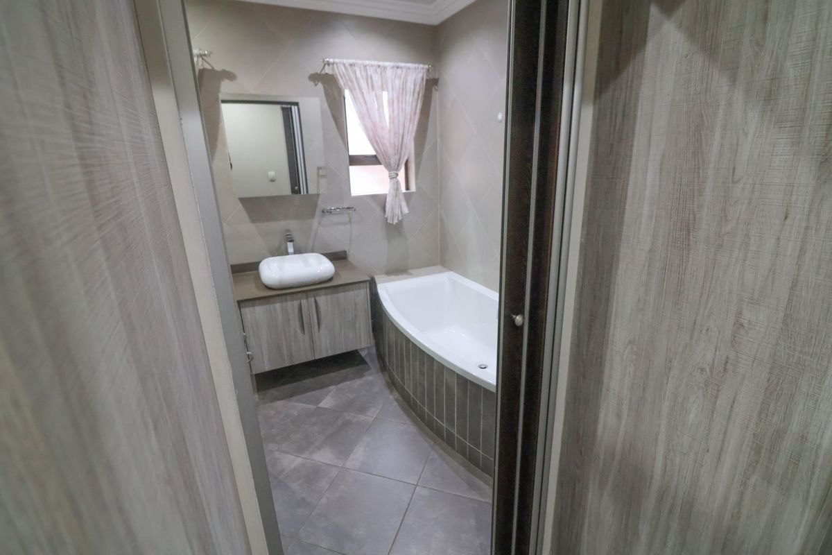 A clean, modern bathroom featuring a vessel sink vanity, a built-in bathtub with tiled surround, and neutral wall and floor tiling.